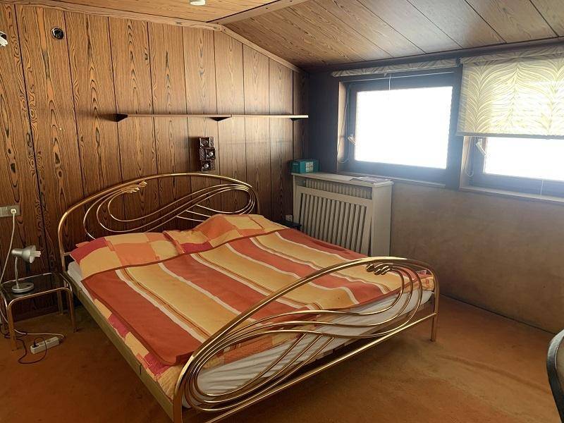 Schlafzimmer mit Holzvertäfelung, Metallbett und Fenster mit Ausblick.
