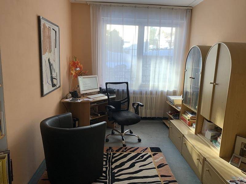 Kleines Arbeitszimmer mit Schreibtisch, Fenster und Teppichboden.