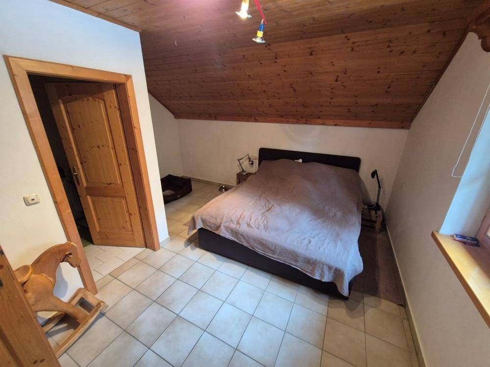Schlafzimmer im Dachgeschoss mit Doppelbett, Fliesenboden und Holzdecke unter der Dachschräge.