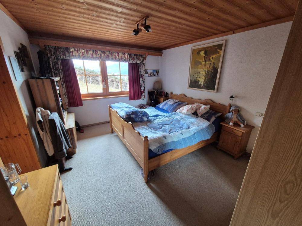 Schlafzimmer mit Doppelbett, Teppichboden und Holzdecke, hell durch ein großes Fenster.