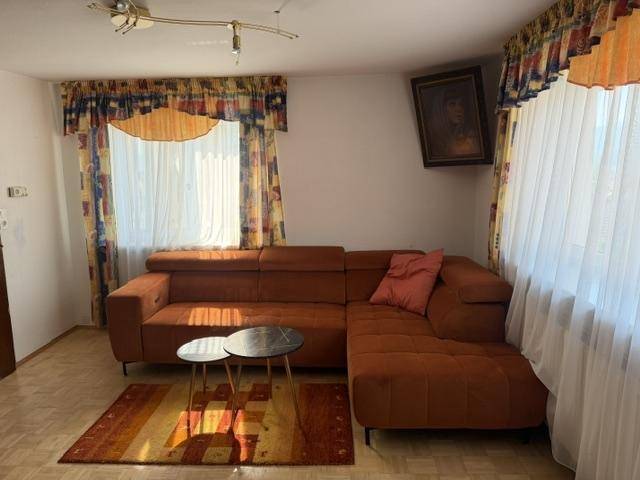 Gemütliches Wohnzimmer mit braunem Ecksofa, Couchtischen und farbenfrohen Vorhängen.