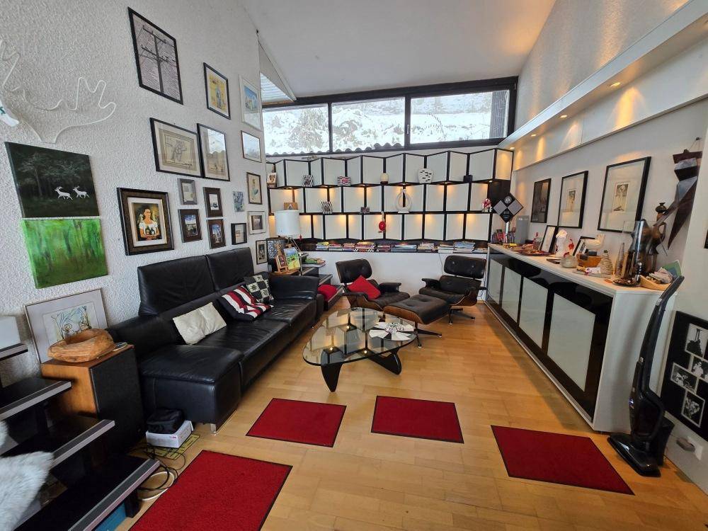 Helles Wohnzimmer mit Holzboden, vielen Bildern an der Wand und einer gemütlichen Sitzecke.