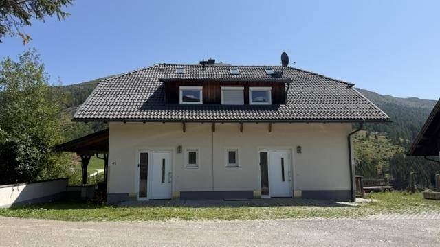 Vorderansicht des Hauses mit zwei Eingängen und Dachgauben, umgeben von Natur.
