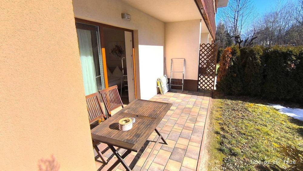 Geräumige Terrasse mit Holztisch und Stühlen, umgeben von Grünflächen und Hecken.