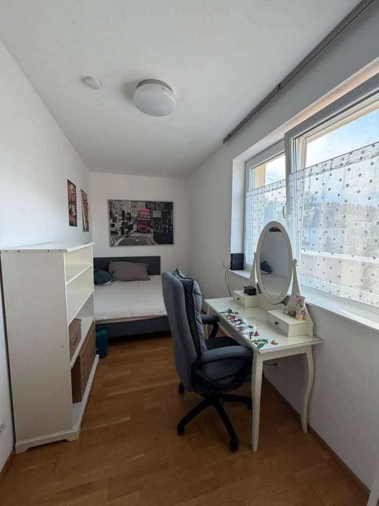 Helles Schlafzimmer mit Holzboden, Schreibtisch und Fenster, ideal als Arbeits- oder Gästezimmer.
