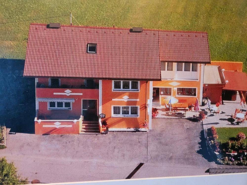 Luftaufnahme eines Gebäudekomplexes mit rotem Dach und umliegender grüner Landschaft.
