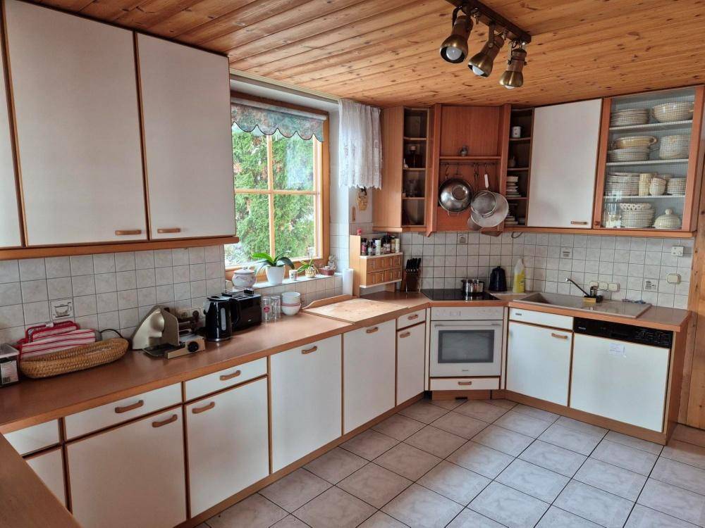 Geräumige Küche mit weißen Schränken, Holztheken und Blick ins Grüne durch das Fenster.