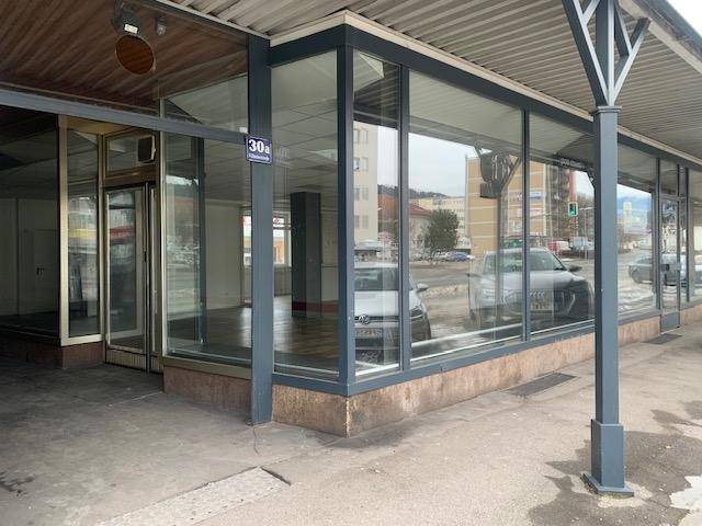 Eingangsbereich und große Schaufenster eines Geschäftsraums im Erdgeschoss mit viel Glas und Blick auf die Straße.