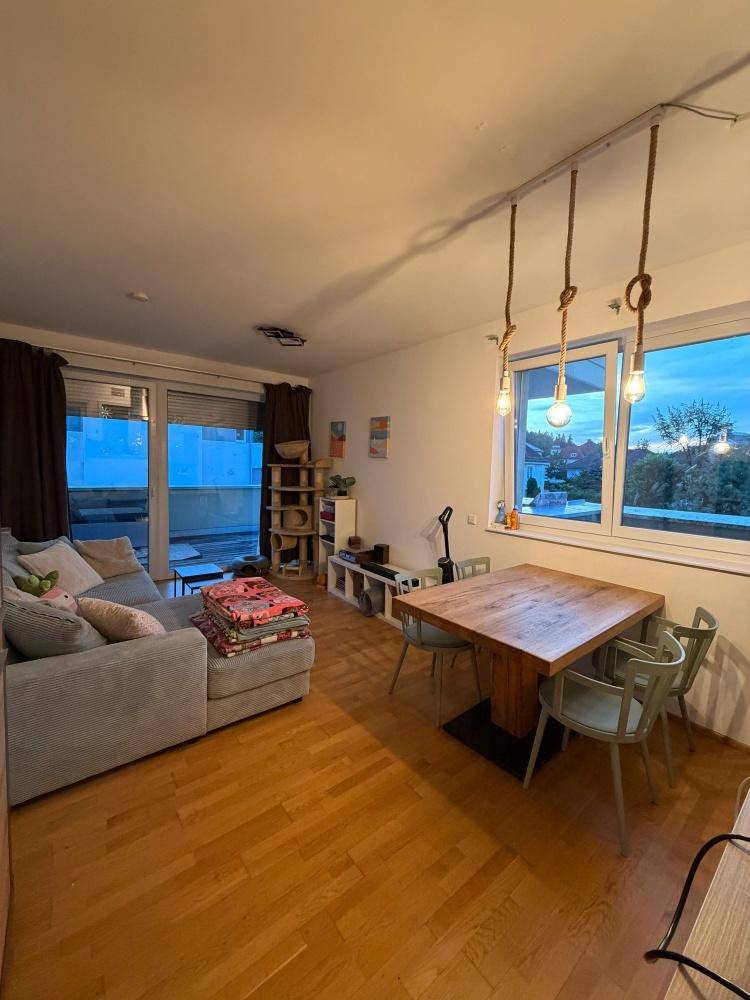 Gemütlicher Wohn-Essbereich mit Holzboden, Esstisch und Zugang zu einem Balkon oder einer Terrasse.