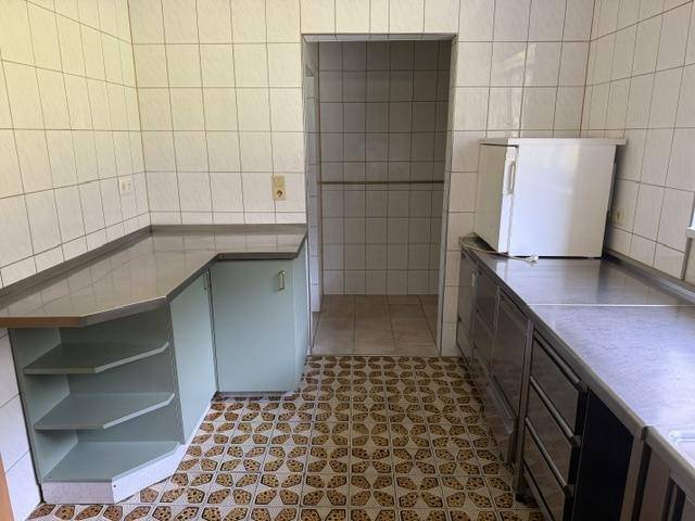 Gewerbliche Küche mit Edelstahl-Arbeitsflächen, Fliesenwänden und einem Durchgang zu einem weiteren Bereich.