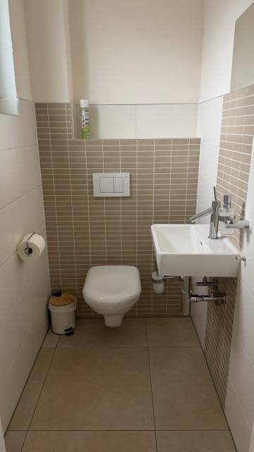 Gäste-WC mit wandhängender Toilette, kleinem Waschbecken und modernen Fliesen.