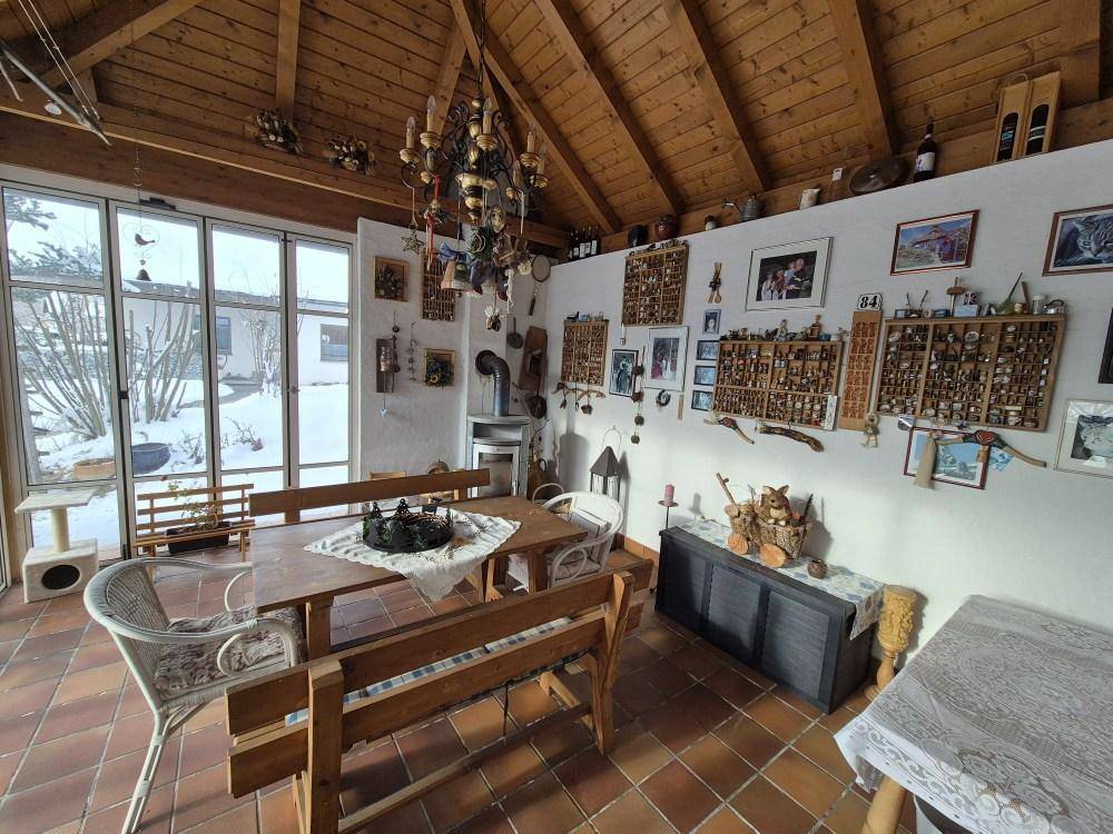 Heller Wintergarten mit Esstisch, Fliesenboden und Blick auf die verschneite Landschaft.