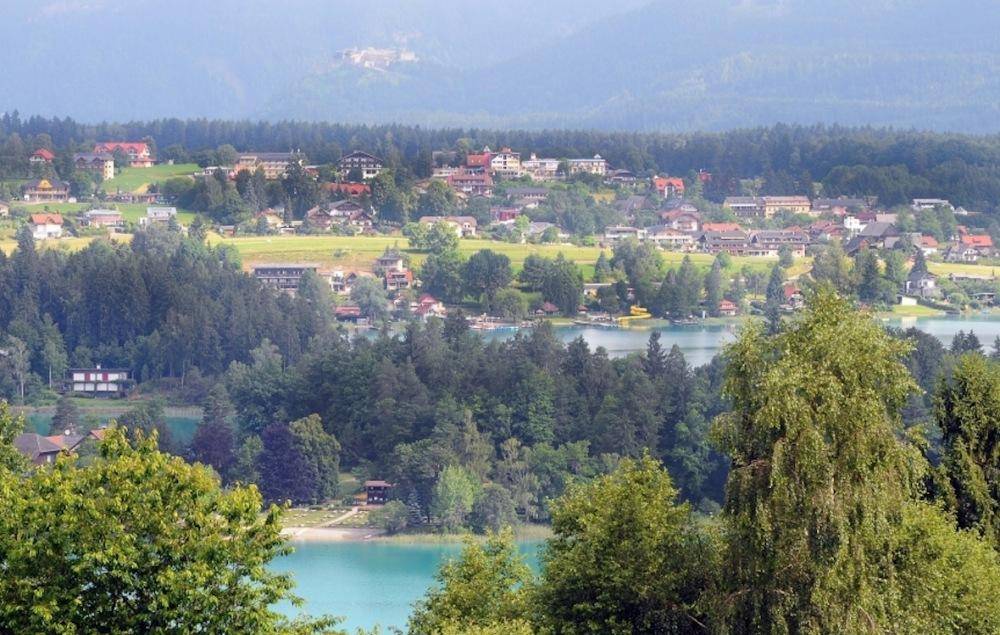 Malerischer Fernblick auf einen See und eine Siedlung, umgeben von grünen Hügeln.