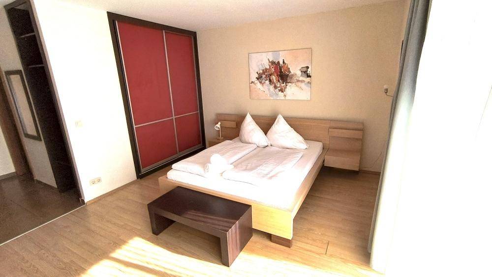 Gemütlicher Schlafbereich mit Doppelbett, Holzboden und großem roten Kleiderschrank.