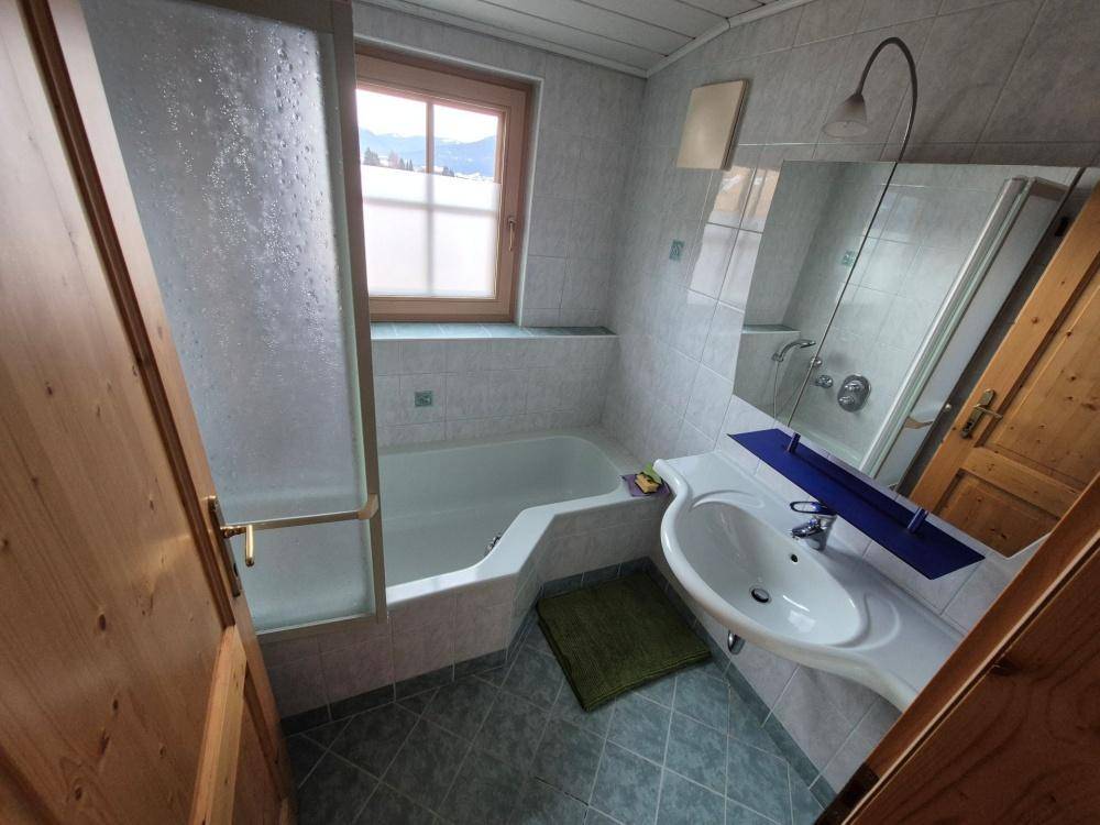 Badezimmer mit Badewanne, Duschabtrennung, Waschbecken und Fenster mit Bergblick.