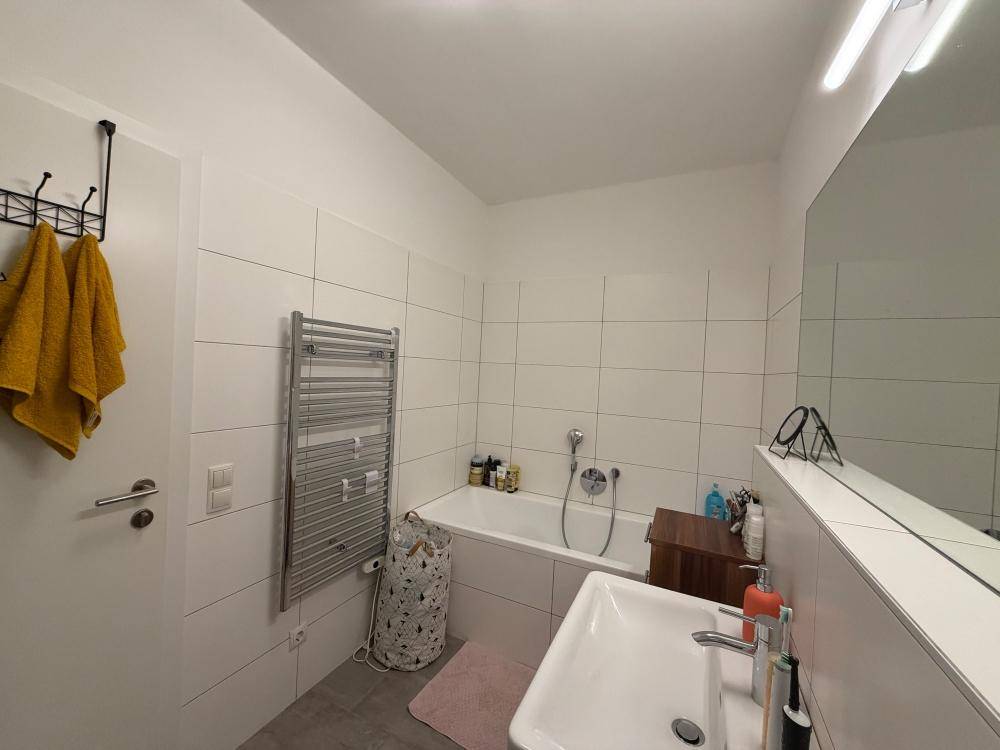 Helles Badezimmer mit Badewanne, Waschbecken, großem Spiegel und beheiztem Handtuchhalter.