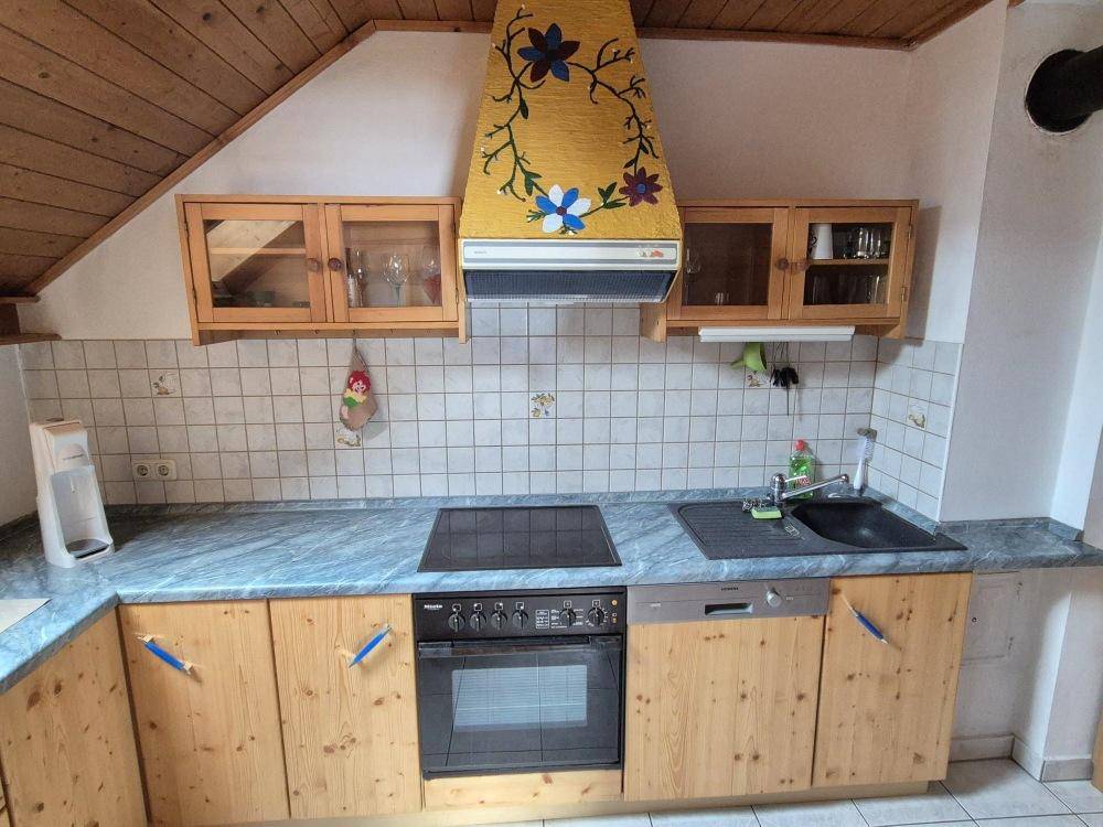 Rustikale Küche mit Holzschränken, blauer Arbeitsplatte und einer floral bemalten Dunstabzugshaube.
