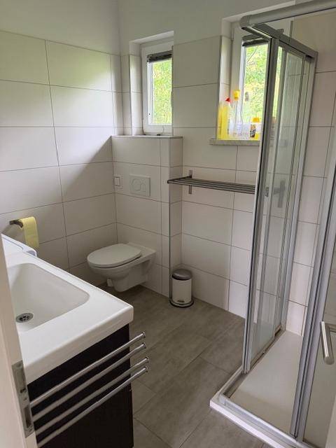 Modernes Badezimmer mit Dusche, WC, Waschbecken und Fenster.