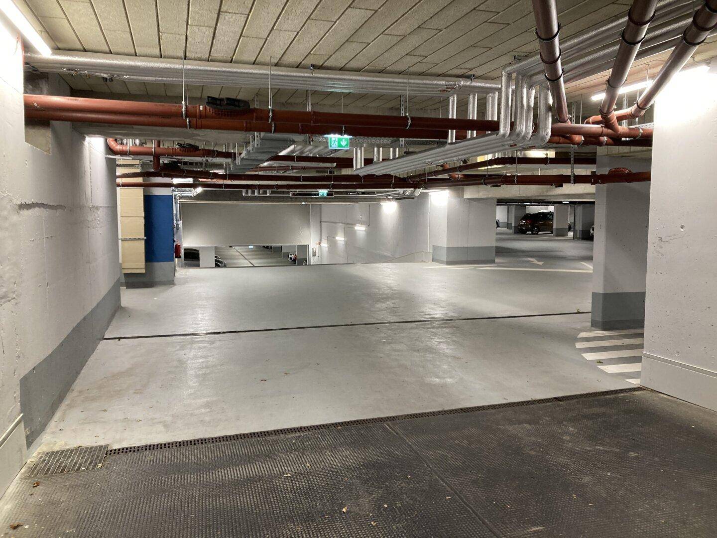 Geräumige Tiefgarage mit vielen Parkplätzen, Betonboden und sichtbaren Installationen an der Decke.
