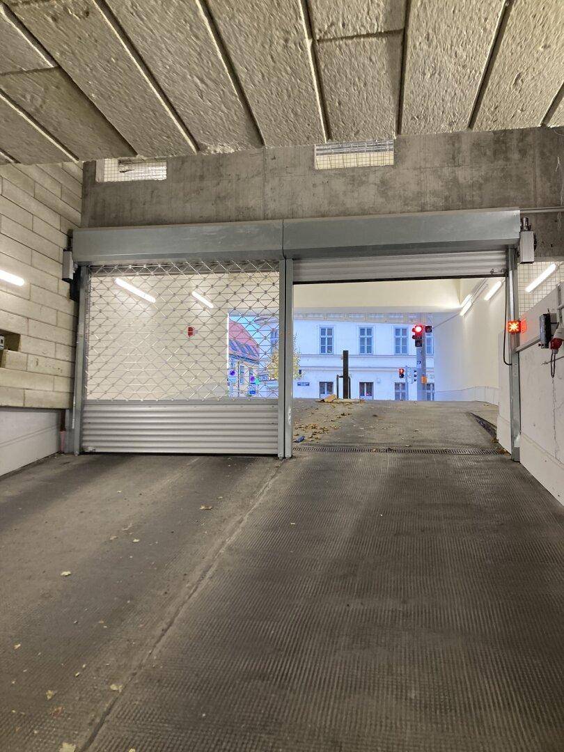 Blick aus der Tiefgaragenausfahrt auf die Straße mit einem teilweise geschlossenen Rolltor und Ampel.