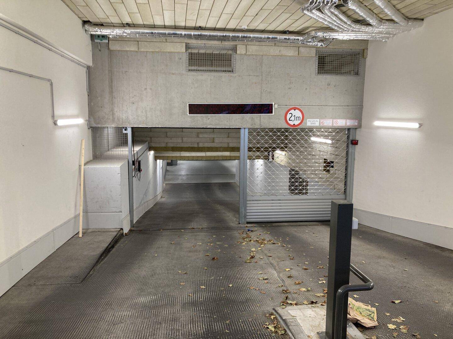 Ausfahrt einer Tiefgarage mit teilweise geöffnetem Rolltor und Laub auf dem Boden.