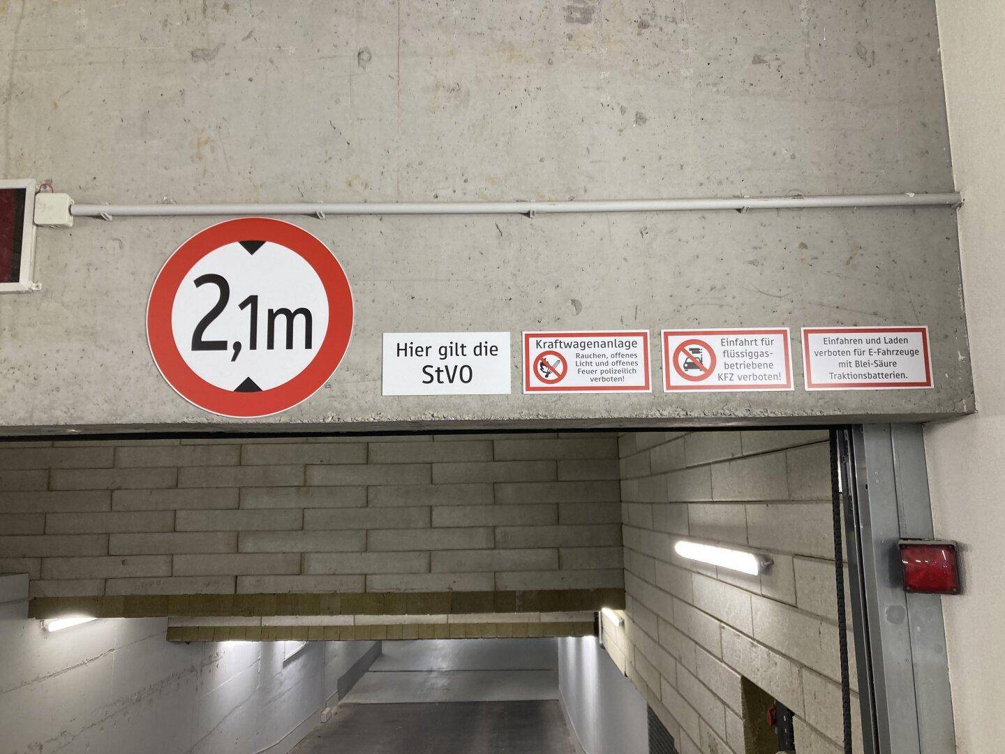 Eingang zu einer Tiefgarage mit Höhenbegrenzungsschild (2,1m) und weiteren Hinweisschildern.