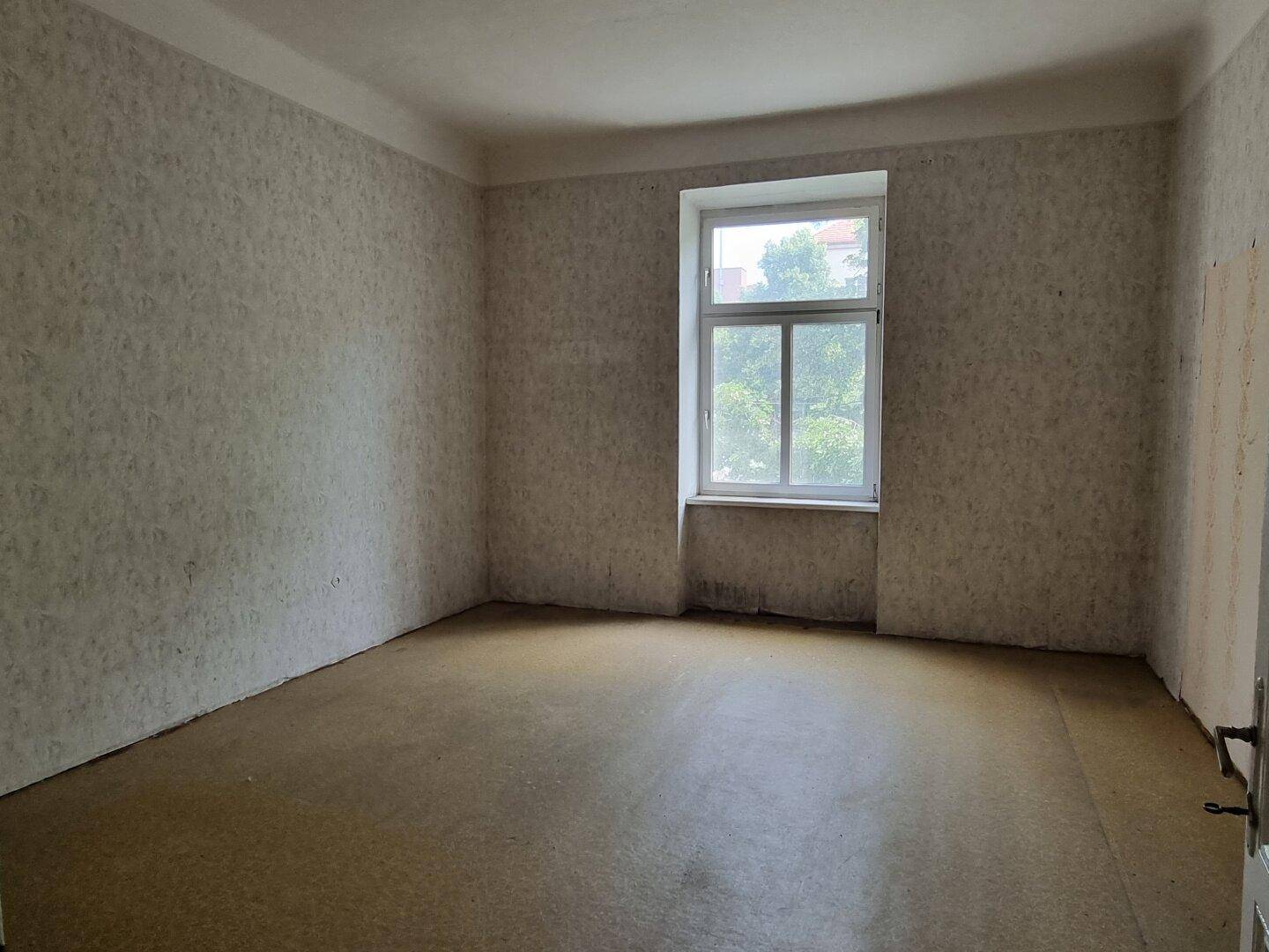 Leerer Raum mit alter Tapete und Fenster, bereit für eine Renovierung.