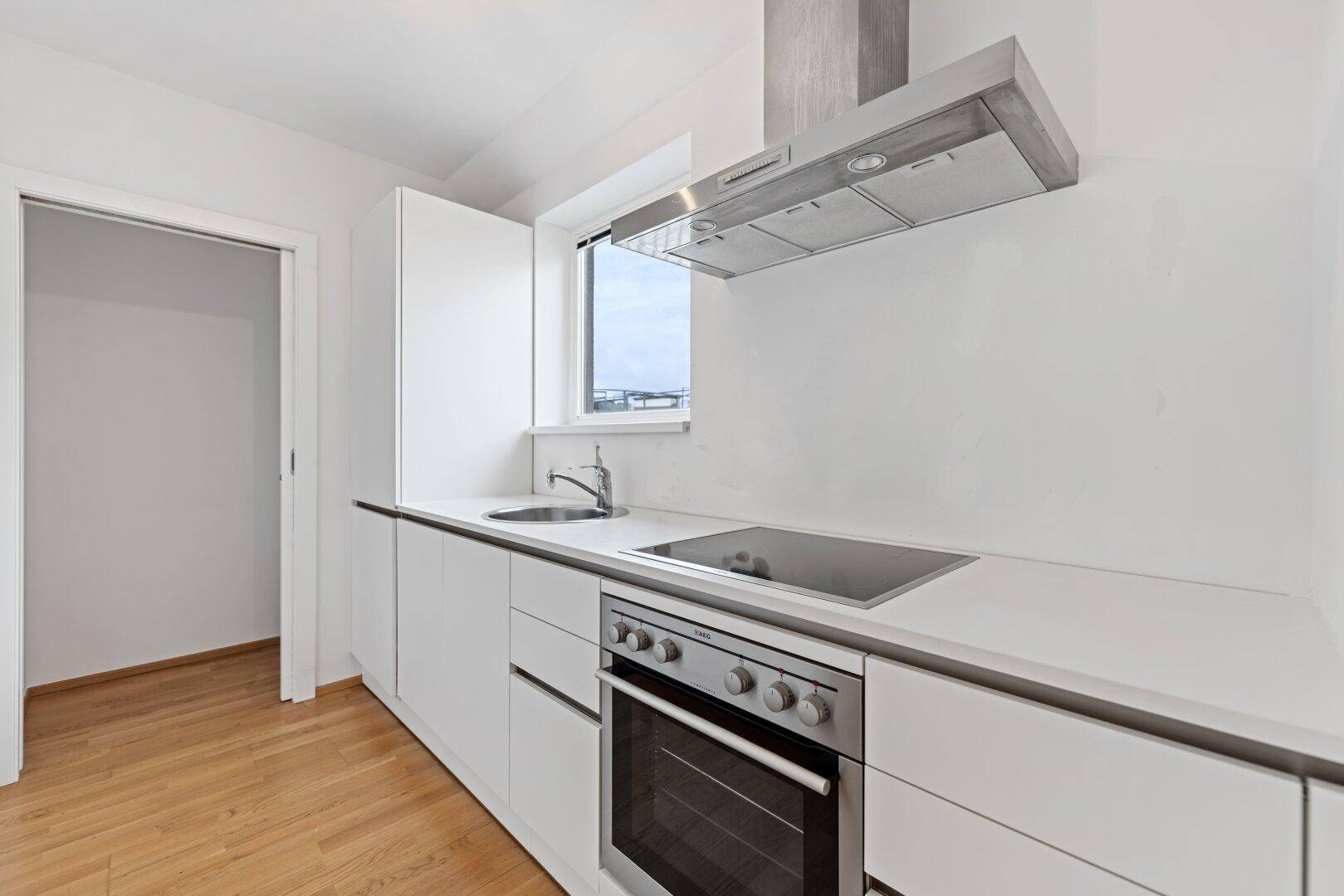 Moderne Einbauküche mit weißen Hochglanzfronten, Induktionskochfeld, Backofen und Dunstabzugshaube.