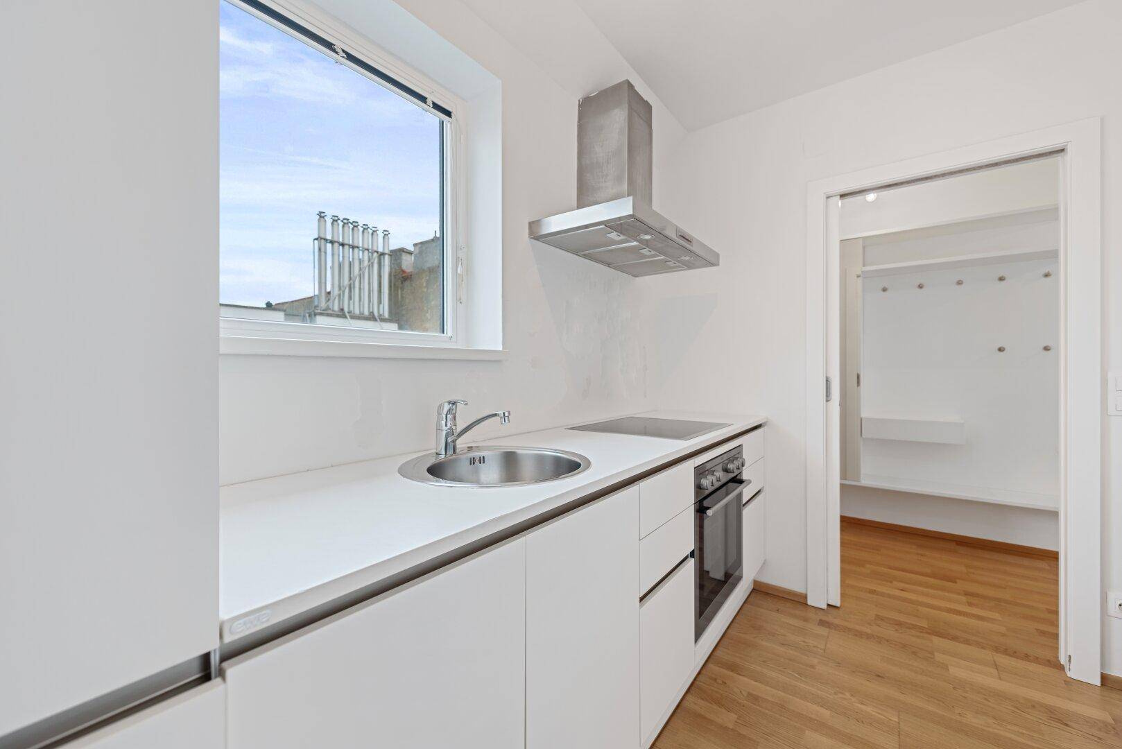 Funktionale Küche mit Edelstahlspüle, weißen Arbeitsplatten und einem Fenster mit Blick nach draußen.