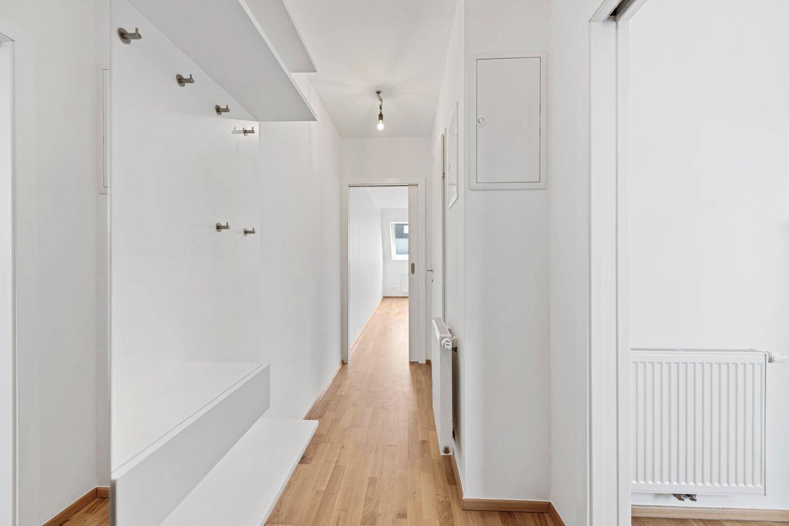 Heller Flur mit Holzboden, einer schlichten Garderobe und Zugang zu weiteren Zimmern der Wohnung.
