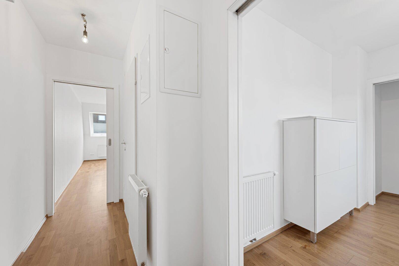 Weiß gestrichener Flur mit Heizkörper und einem weißen Schrank, der zu anderen Räumen führt.