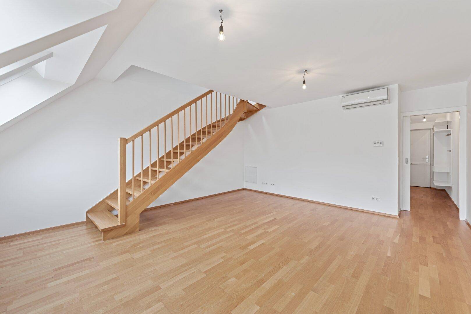 Geräumiges Dachgeschosszimmer mit Holztreppe, Klimaanlage und hellem Parkettboden.