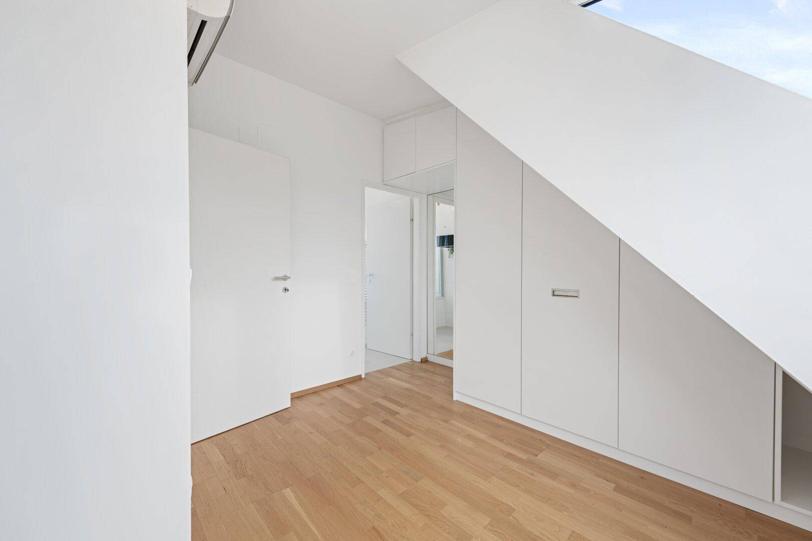 Dachgeschosszimmer mit Parkettboden, praktischen Einbauschränken und Zugang zum Badezimmer.