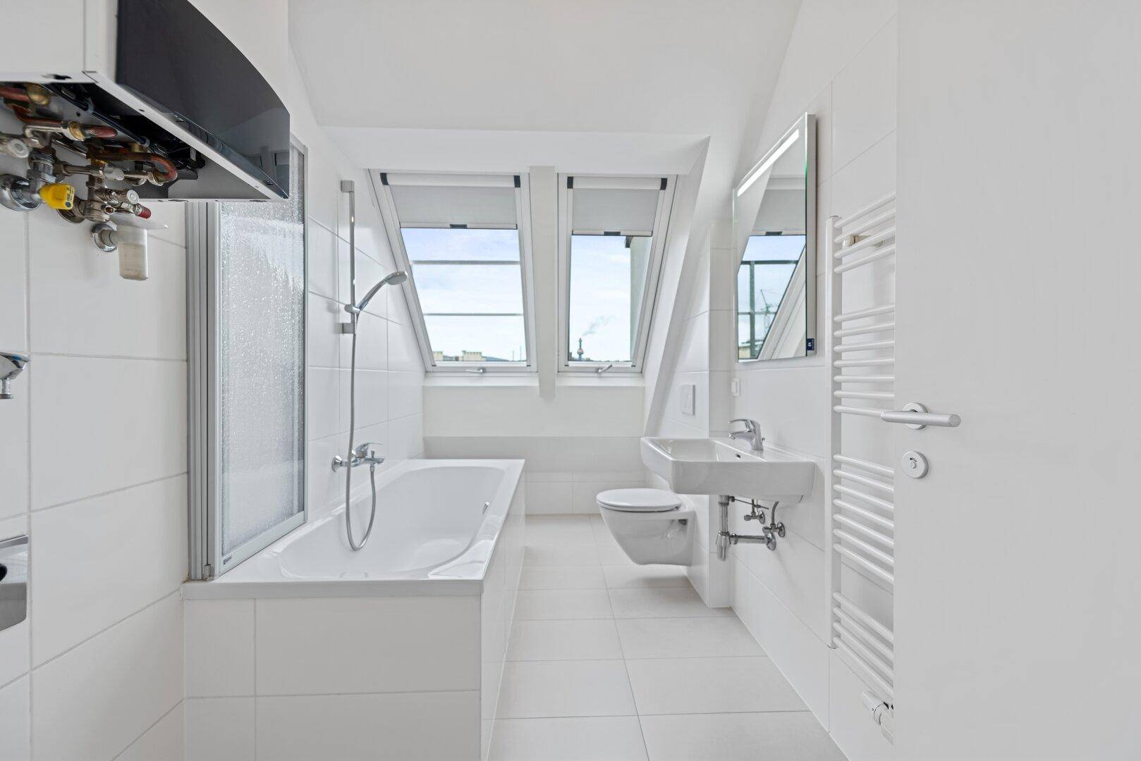 Helles Badezimmer mit weißen Fliesen, Badewanne, WC und einem praktischen Handtuchheizkörper.