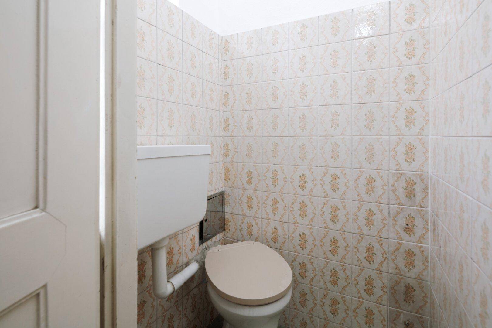 Kleine Gästetoilette mit WC und gemusterten Fliesen im Retro-Stil.