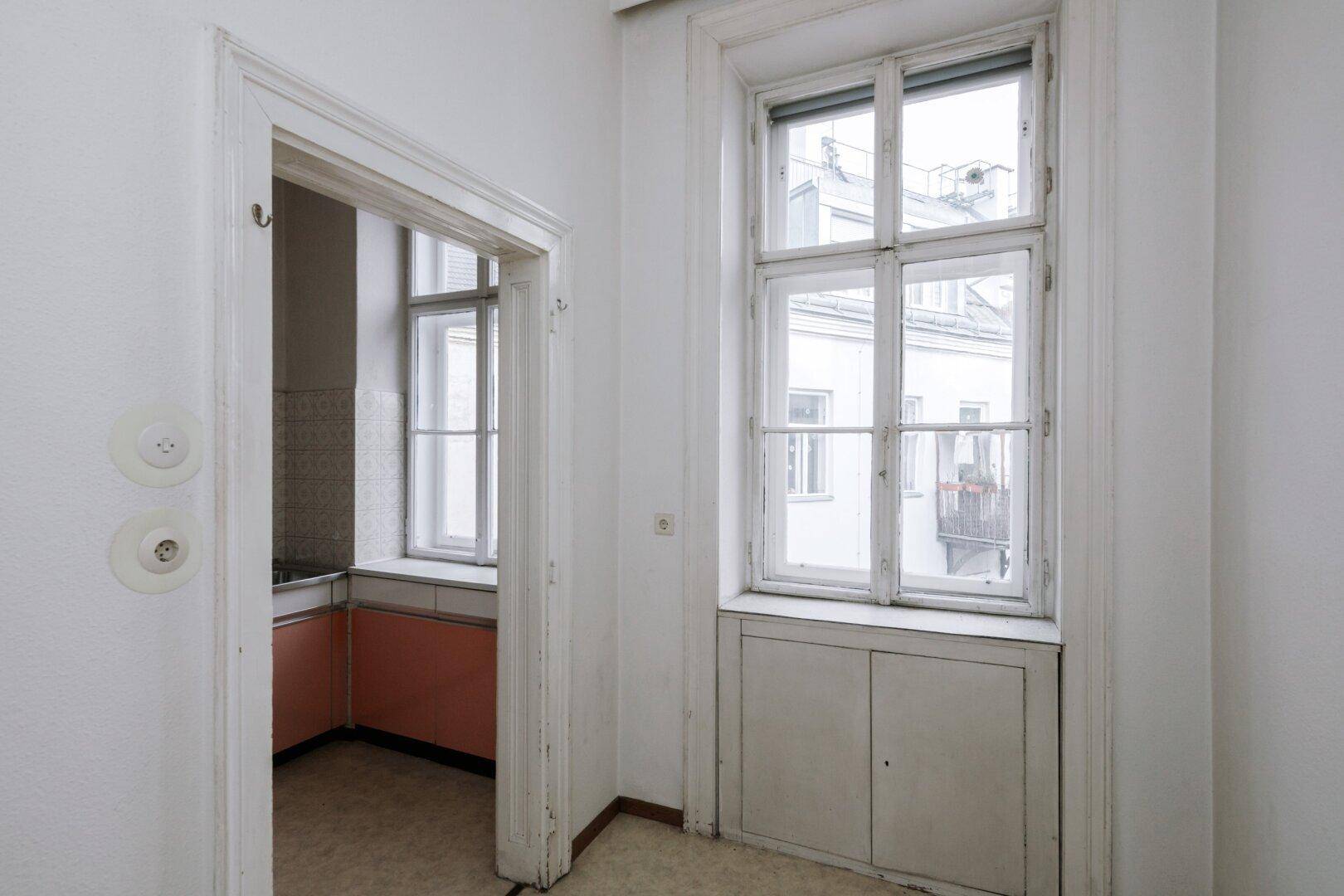 Flurbereich mit Blick in eine Küche im Vintage-Stil und einem Fenster mit Stauraum darunter.