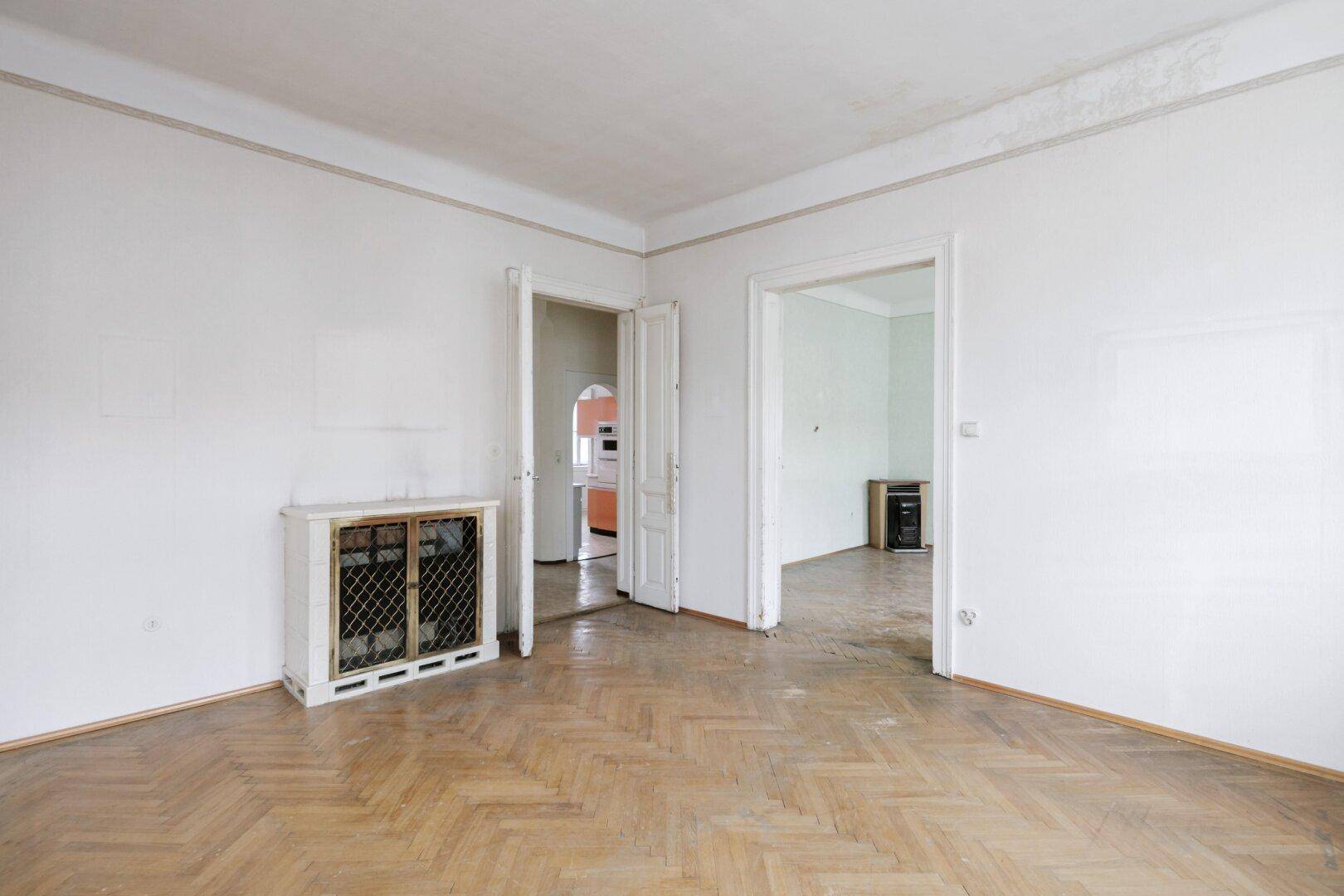 Helles Zimmer mit Fischgrätparkett und Blick in die Küche und einen weiteren Raum.