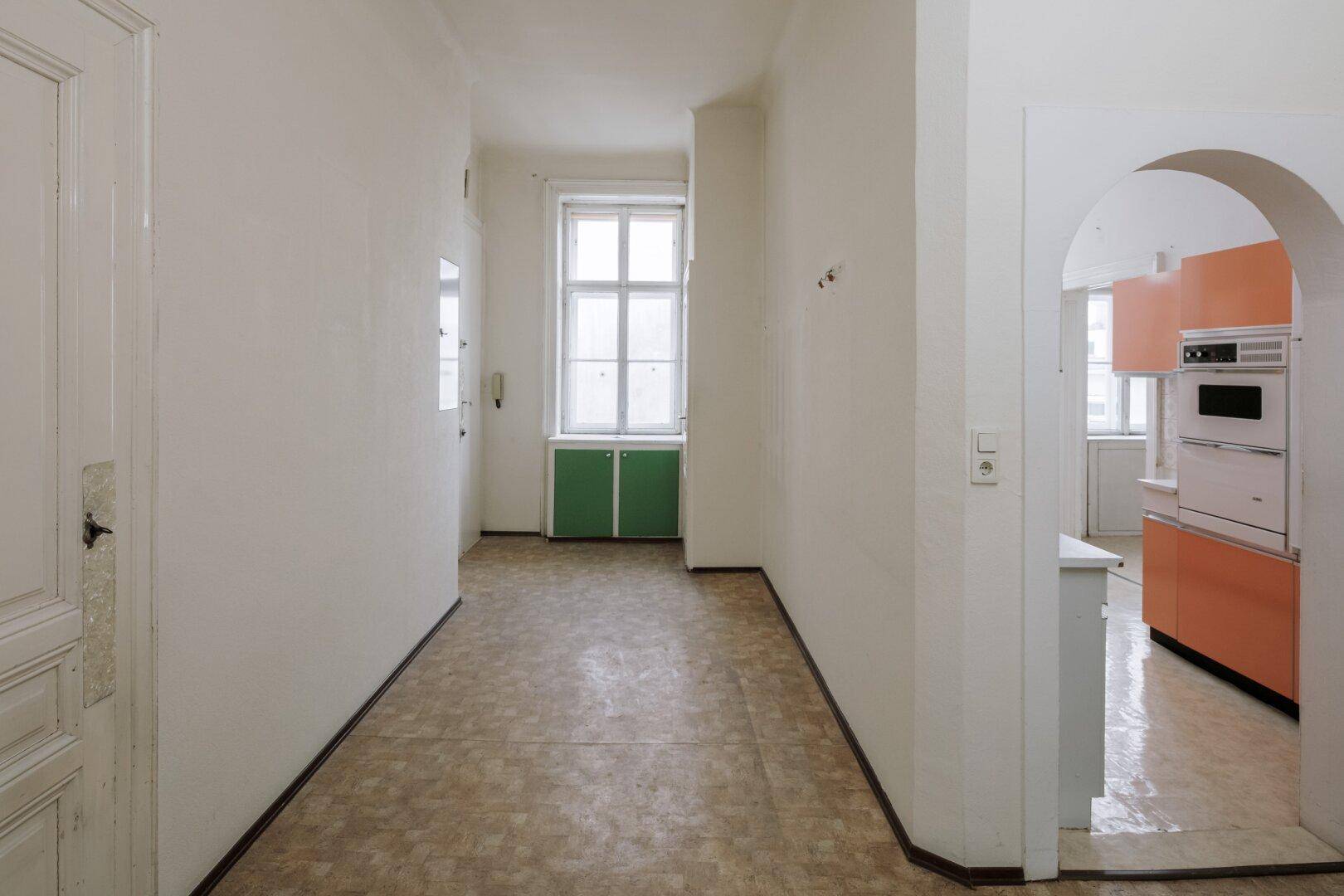 Langer Flur mit PVC-Boden und Blick in die Küche durch einen Rundbogen.