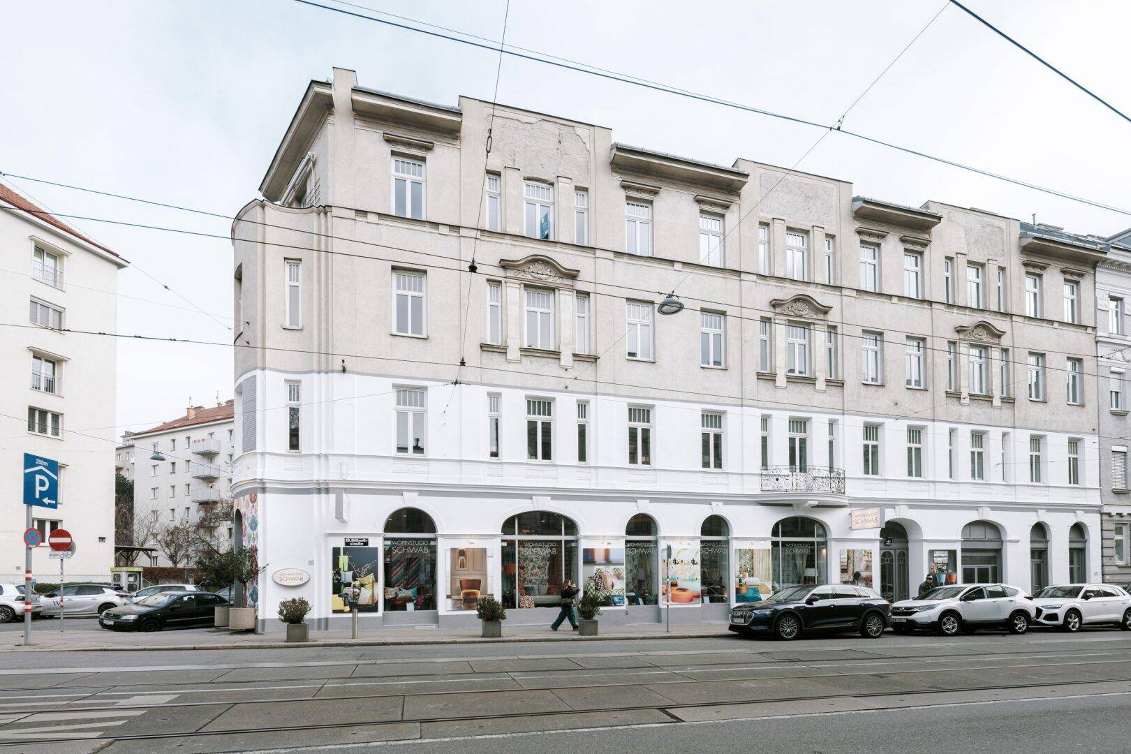 Historisches Eckgebäude mit Geschäften im Erdgeschoss und Blick auf die Stadtstraße.