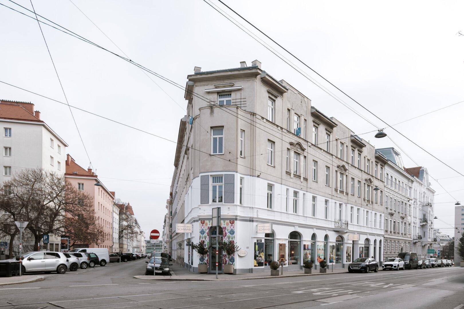 Historisches Eckgebäude mit Geschäften im Erdgeschoss und Blick auf die Stadtstraße.