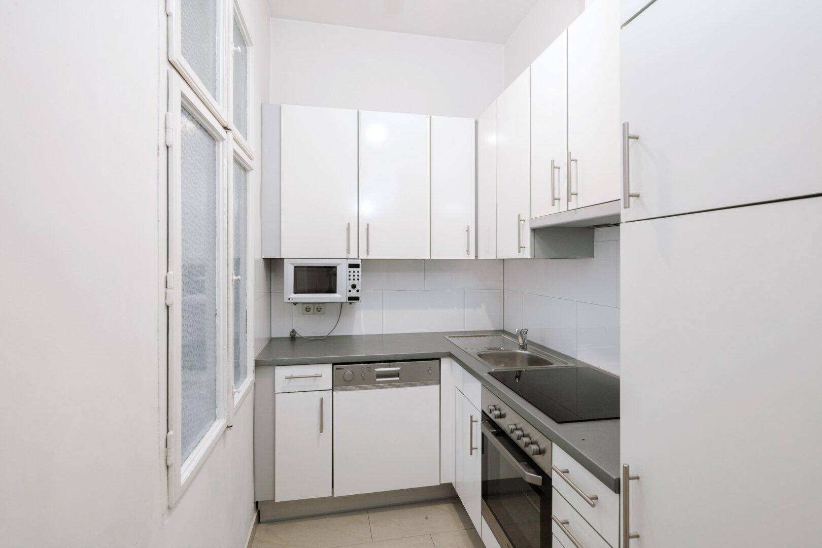 Funktionale Küche mit weißen Hochglanzschränken, integrierten Geräten und Fenster.
