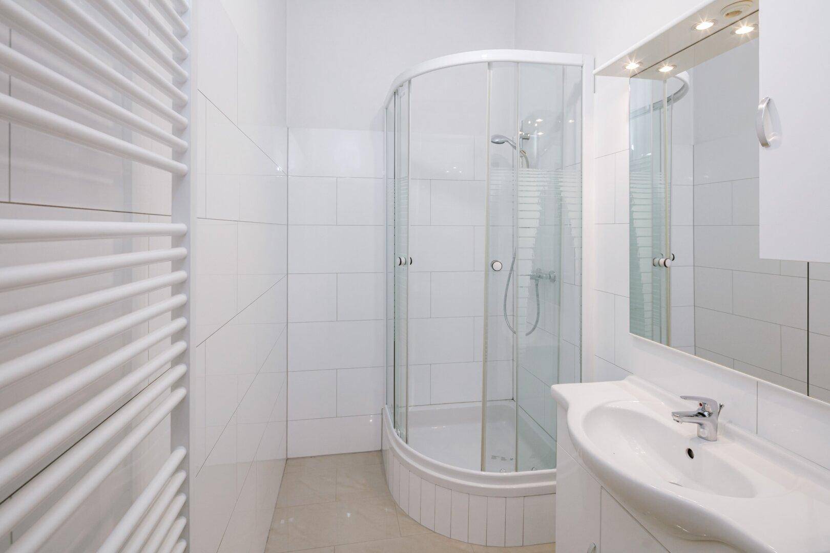 Modernes Badezimmer mit Duschkabine, Waschbecken und beheiztem Handtuchhalter.
