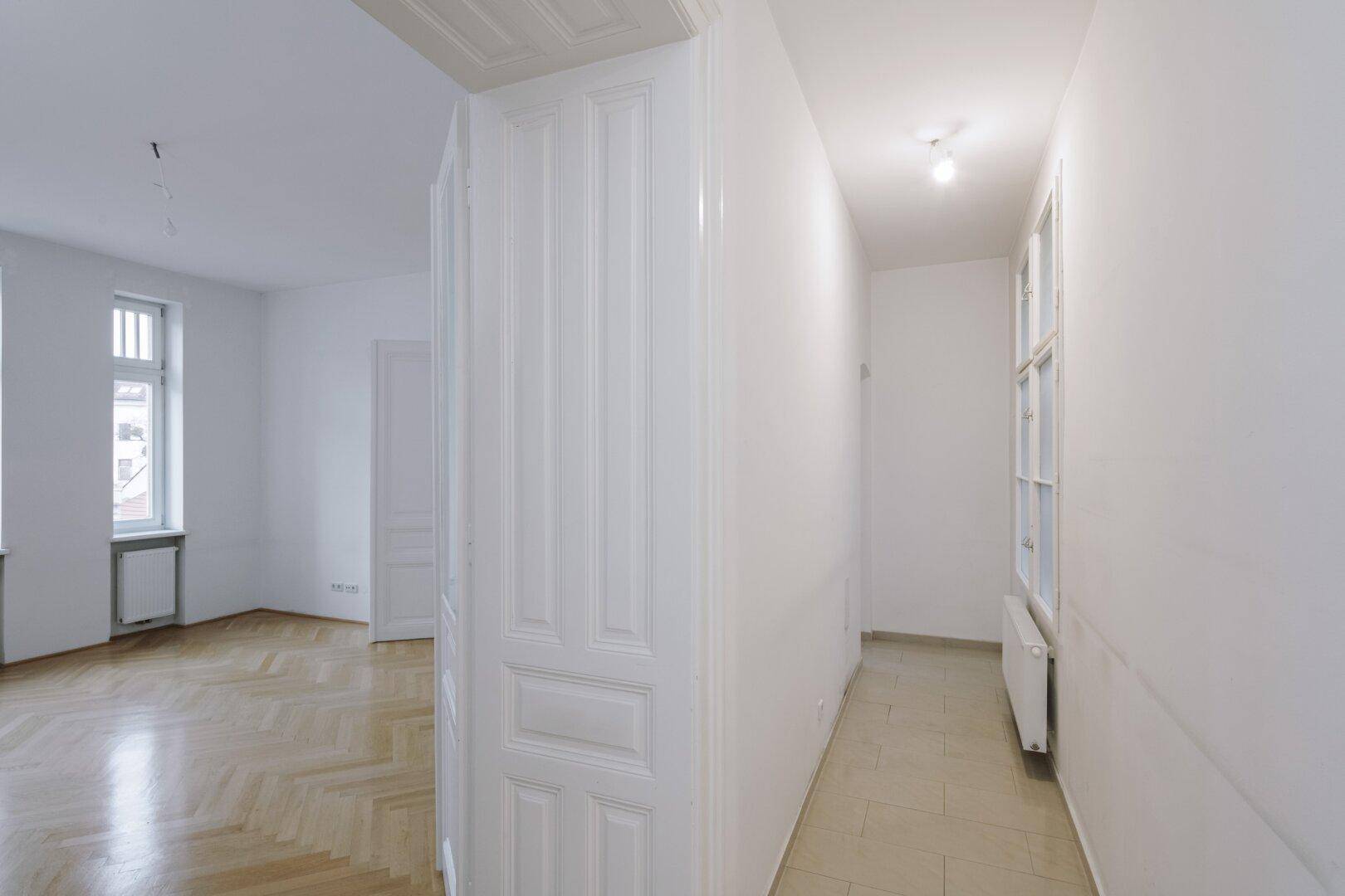 Langer Flur mit Fliesenboden und Blick in ein Zimmer mit Parkett.