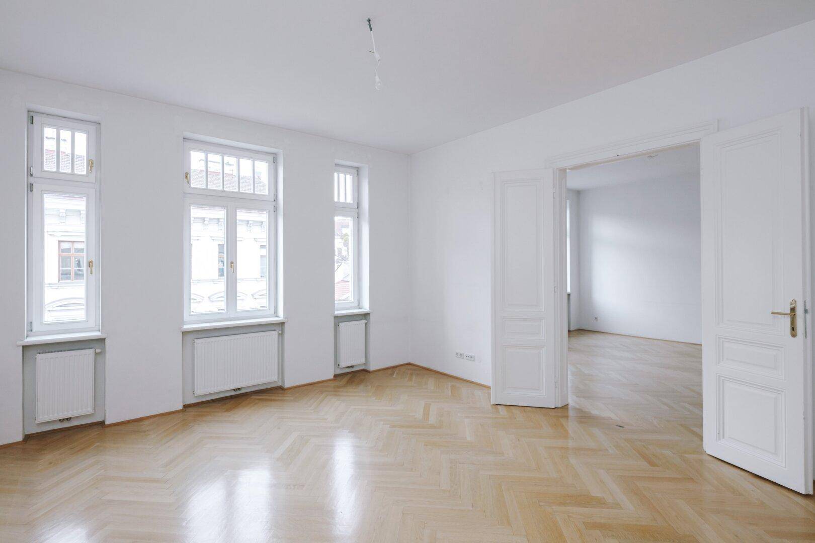 Geräumiges Zimmer mit Fischgrätparkett und hohen Fenstern, bereit zur individuellen Gestaltung.