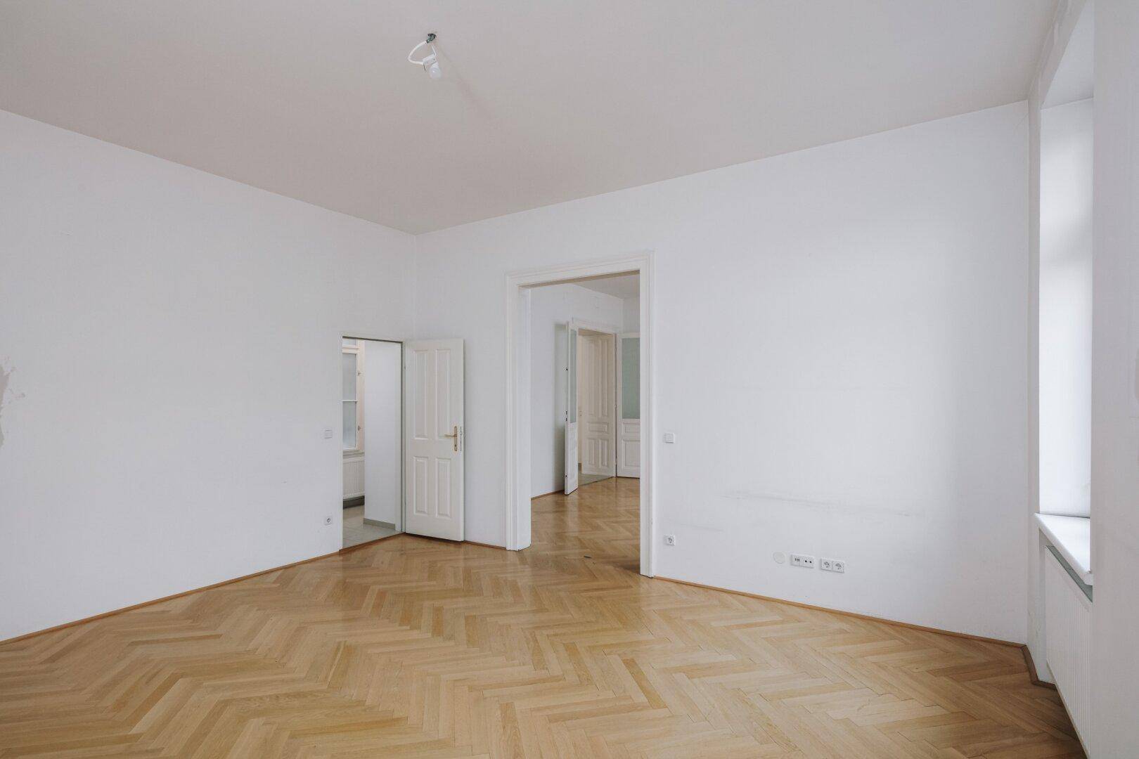 Geräumiges Zimmer mit Fischgrätparkett und Zugang zu weiteren Räumen.