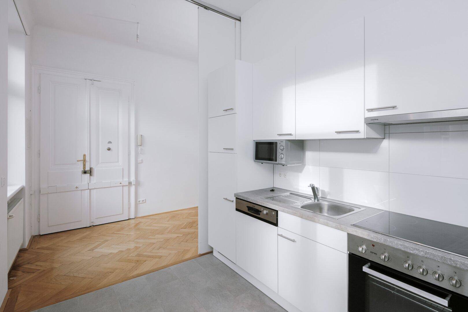 Helle Einbauküche mit Mikrowelle, Spülmaschine und Blick auf die Eingangstür der Wohnung.