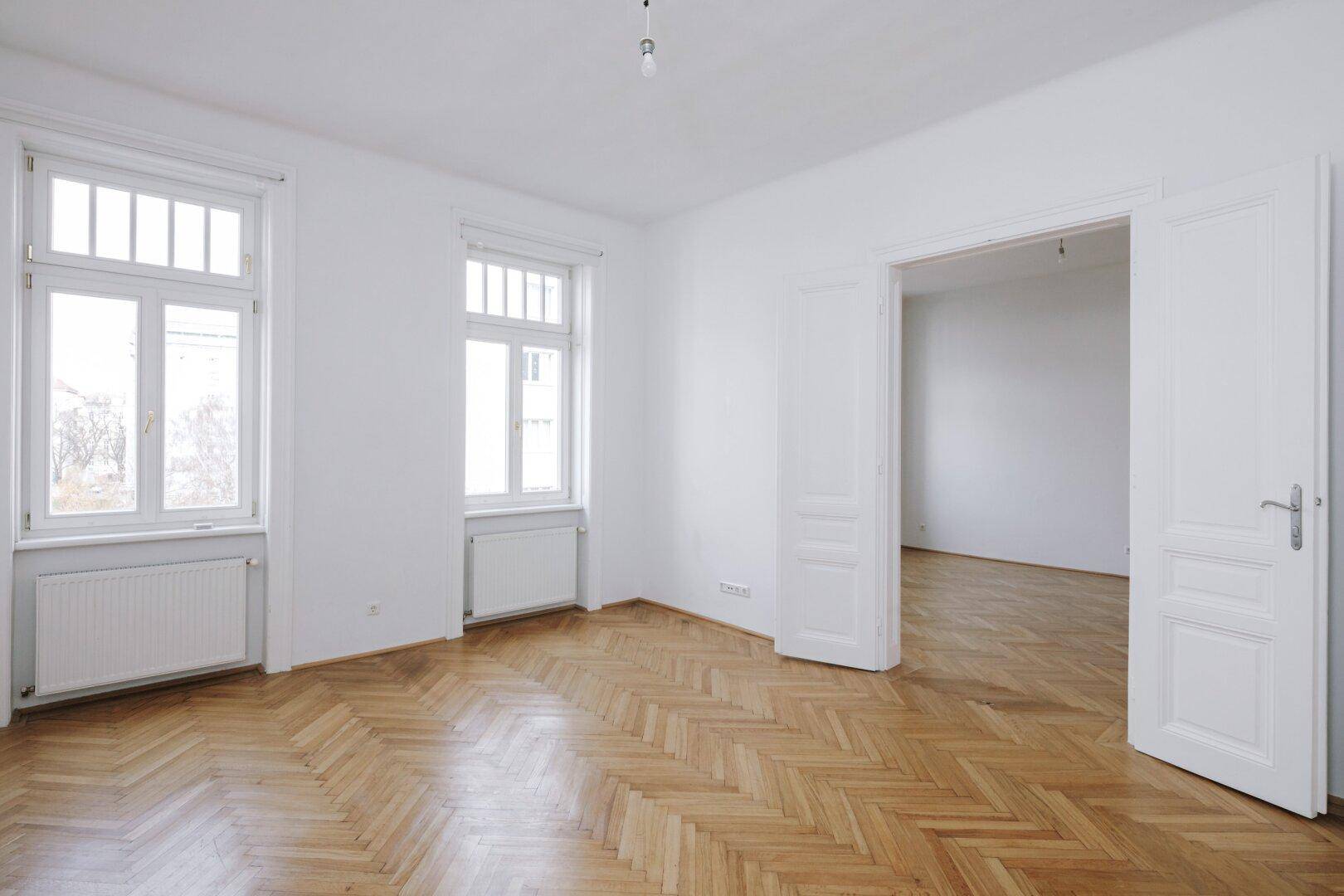 Geräumiges Zimmer mit Fischgrätparkett und hohen Flügeltüren, die zu angrenzenden Räumen führen.