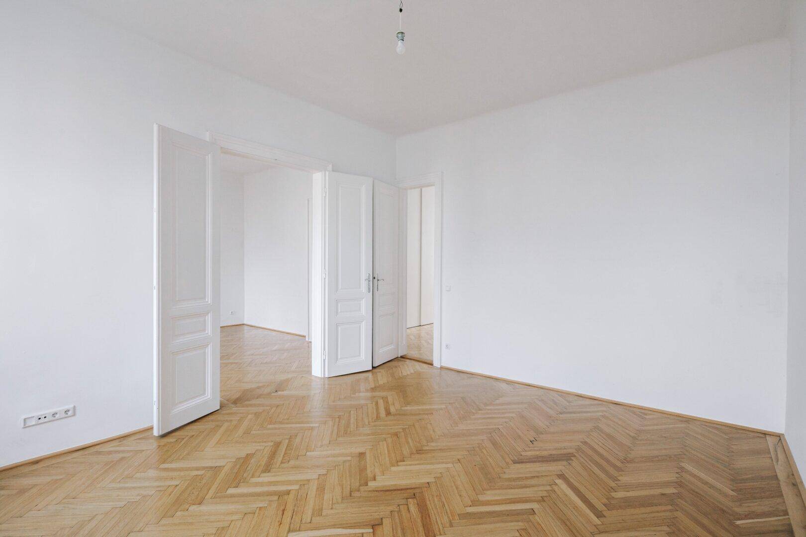Geräumiges Zimmer mit Fischgrätparkett und doppelten Flügeltüren zu angrenzenden Räumen.