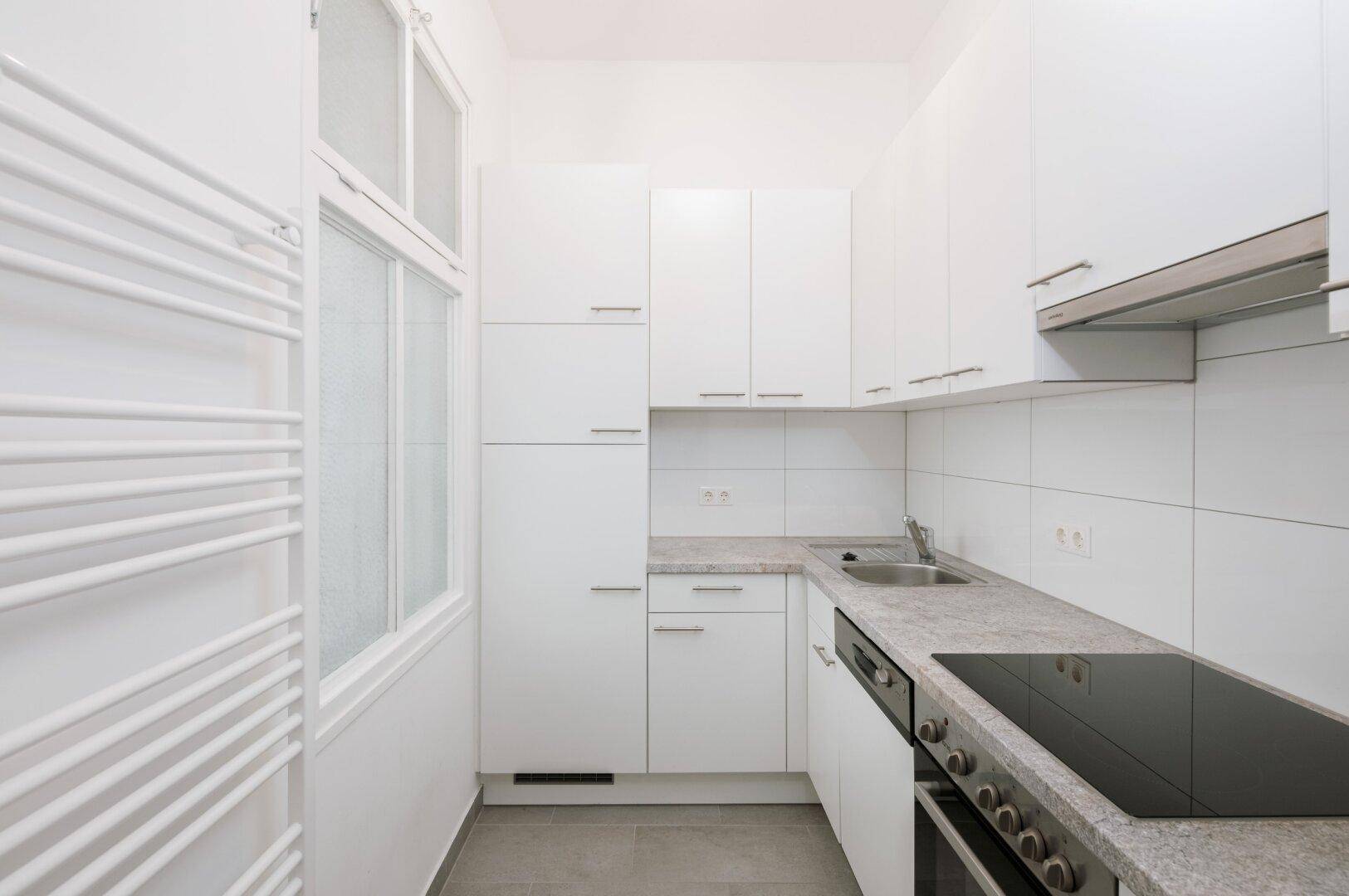 Moderne, schmale Küche mit weißen Schränken, Induktionskochfeld und Fenster.
