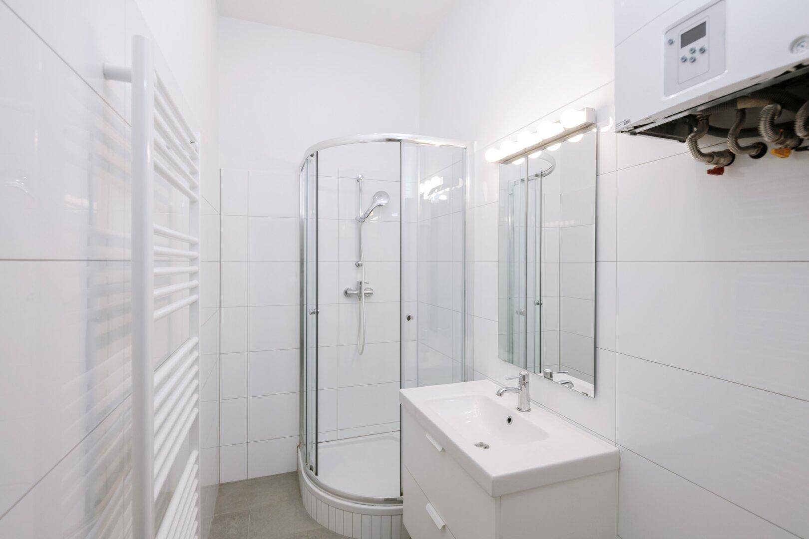 Helles Badezimmer mit Duschkabine, Waschbecken und Handtuchheizkörper.